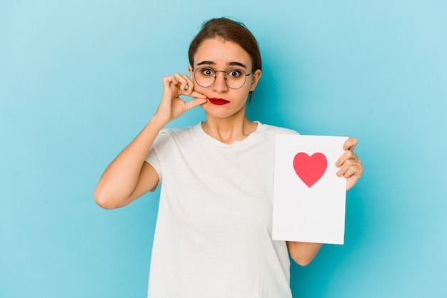 Giovane ragazza araba magra che tiene una carta di San Valentino con le dita sulle labbra mantenendo un segreto.