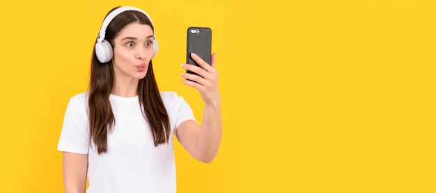 Giovane ragazza ascoltare musica in cuffia tenere il telefono su sfondo giallo selfie Donna faccia isolata