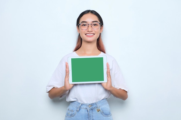 Giovane ragazza asiatica allegra in maglietta bianca che mostra tablet digitale con schermo vuoto isolato su sfondo bianco