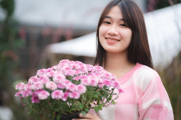 Giovane ragazza asiatica carina che indossa una camicia rosa e tiene in mano un bellissimo fiore rosa ritratto modello femminile con il concetto di natura con fiore rosa in mano felice e sorriso all'aperto