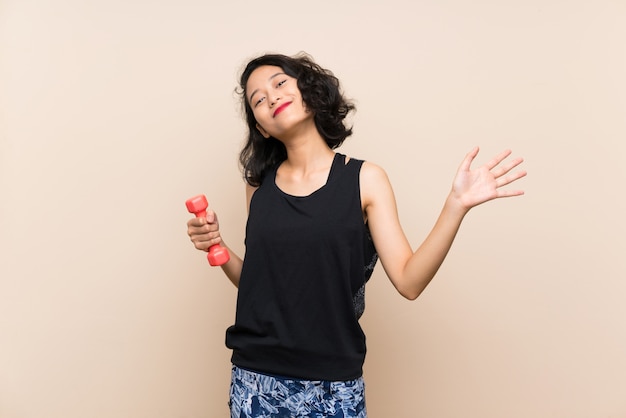 Giovane ragazza asiatica che fa sollevamento pesi sopra il fondo isolato che saluta con la mano con l'espressione felice