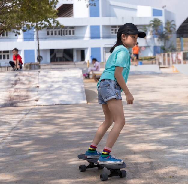 Giovane ragazza asiatica che guida lo skateboard della vecchia scuola in skatepark