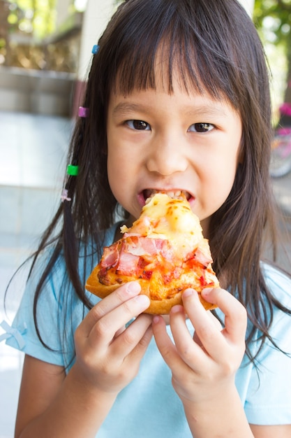 Giovane ragazza asiatica che mangia pizza. Fronte del primo piano e azione attraente. Fast food preferito.