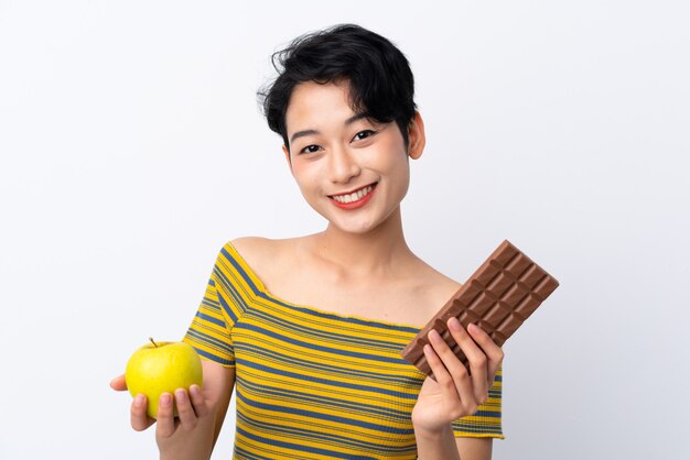 Giovane ragazza asiatica che prende una compressa di cioccolato in una mano e una mela nell'altra