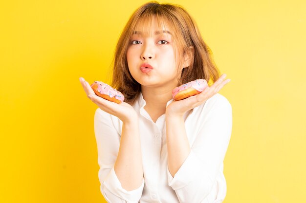 Giovane ragazza asiatica che tiene la ciambella con l'espressione allegra sullo sfondo