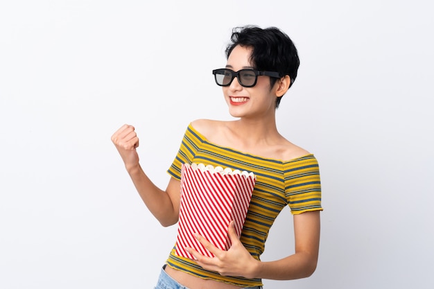 Giovane ragazza asiatica con gli occhiali 3d e in possesso di un grande secchio di popcorn mentre guardando di lato