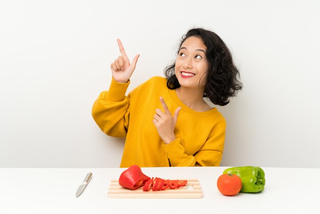 Giovane ragazza asiatica con le verdure in una tabella che indica con il dito indice una grande idea