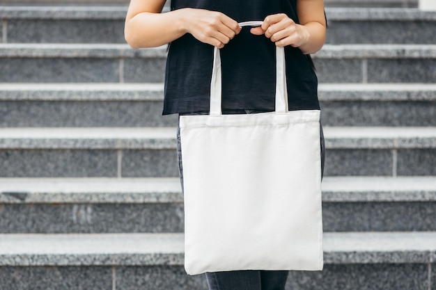 Giovane ragazza asiatica modello vestita con una maglietta bianca per strada con in mano una borsa ecologica bianca