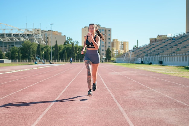 Giovane ragazza atletica con tatuaggi corre intorno a una pista da corsa