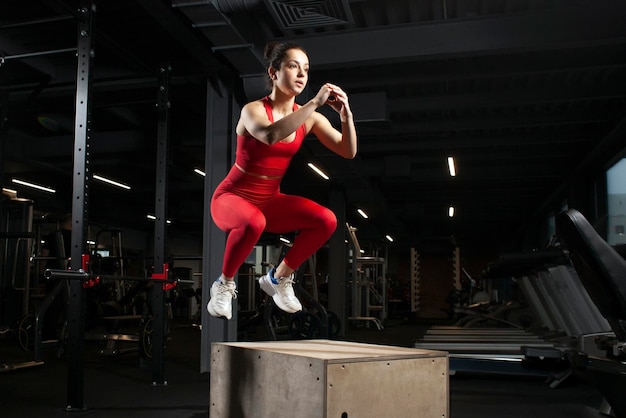 Giovane ragazza atletica in abbigliamento sportivo rosso che salta in palestra nera donna attraente che fa sport