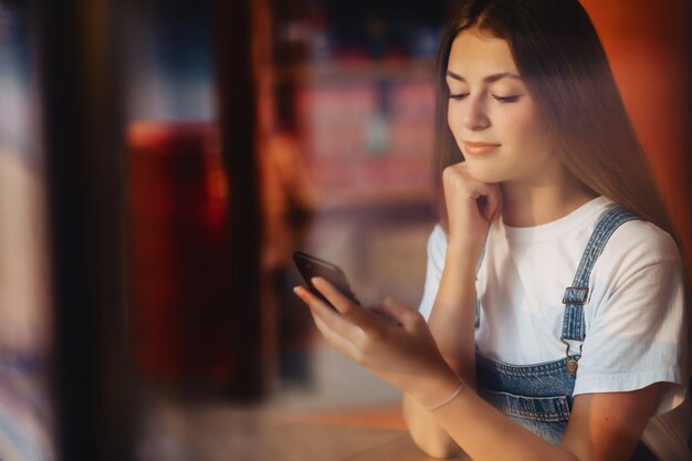 Giovane ragazza attraente attraente al caffè con il vetro di finestra di throuth del telefono e del caffè