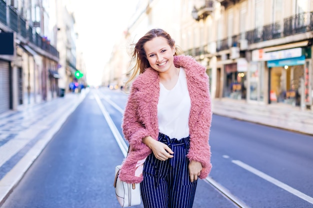 Giovane ragazza attraente che cammina lungo la strada dello shopping lungo la via dello shopping di una città europea nella stagione degli sconti su uno sfondo di boutique sfocate