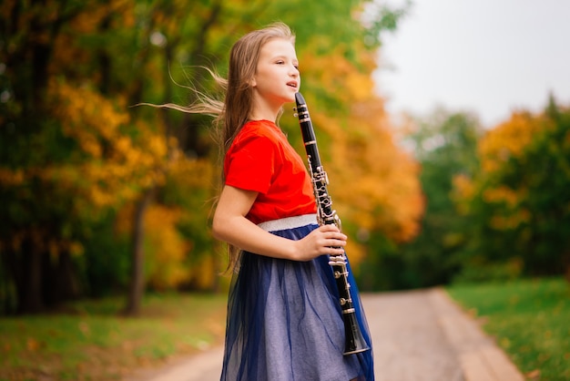 Giovane ragazza attraente che suona il clarinetto, ebano nel parco autunnale