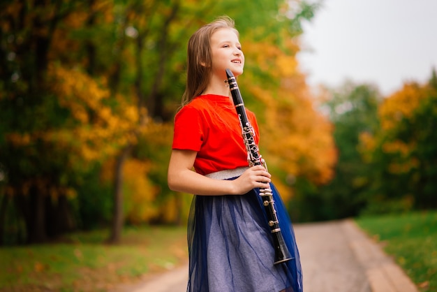 Giovane ragazza attraente che suona il clarinetto, ebano nel parco autunnale