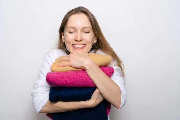 Giovane ragazza attraente che tiene in mano tre maglioni preferiti e sorride ampiamente su sfondo bianco isolato Il concetto di un guardaroba invernale preferito