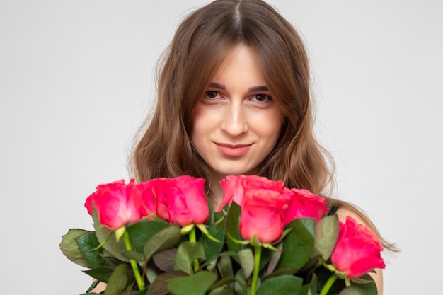 Giovane ragazza attraente con un mazzo di rose rosse su sfondo bianco Una ragazza felice con un mazzo di rose sorride Il concetto di felicità gioia e celebrazione