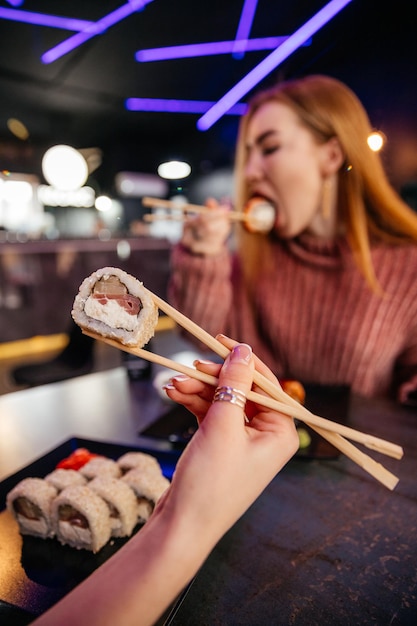 Giovane ragazza attraente in possesso di un rotolo di sushi makizushi servito su piatto nero su sfondo sushibar