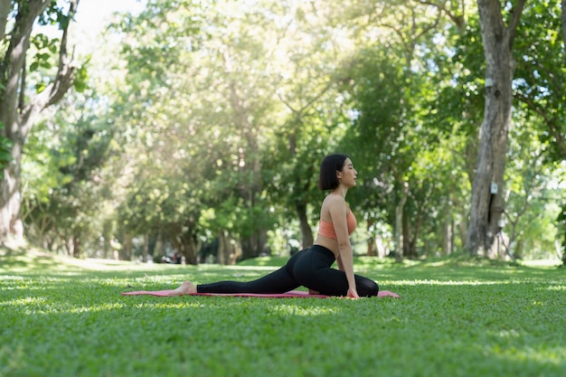 Giovane ragazza attraente sta facendo asana yoga avanzato sul tappetino fitness nel mezzo di un parco