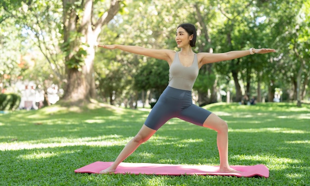 Giovane ragazza attraente sta facendo asana yoga avanzato sul tappetino fitness nel mezzo di un parco