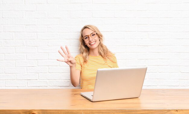 giovane ragazza bionda al laptop mostrando il numero quattro o il quarto con la mano in avanti