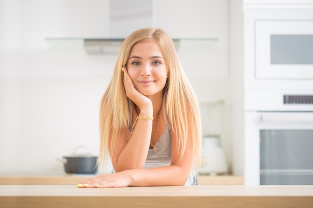 Giovane ragazza bionda allegra nella cucina della casa. Pensa a cosa cucinerà oggi.