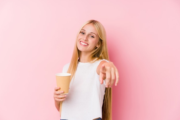 Giovane ragazza bionda che tiene i sorrisi allegri di un caffè asportabile che indicano la parte anteriore.