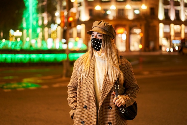 Giovane ragazza bionda con la maschera che guarda al lato. È in una città di notte. Atmosfera invernale.