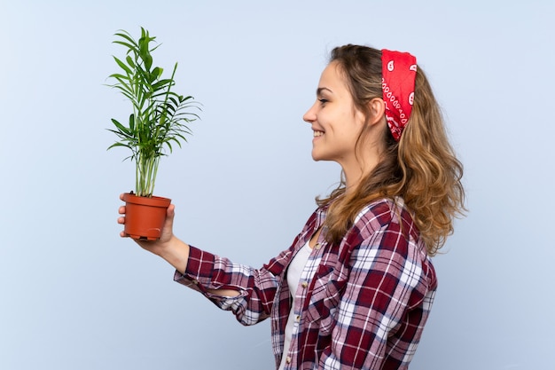 Giovane ragazza bionda del giardiniere che tiene una pianta con l'espressione felice