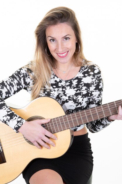 Giovane ragazza bionda sorridente che gioca seduta della chitarra isolata su fondo bianco