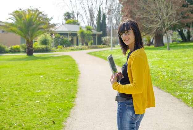 Giovane ragazza bruna con una tavoletta nel parco, fuori