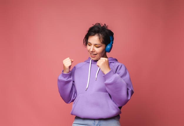 Giovane ragazza bruna in un maglione lilla e cuffie posa in isolamento su uno sfondo rosa in studio Il concetto di stile di vita delle persone Ascolta la musica con le cuffie ritratto in studio di danza