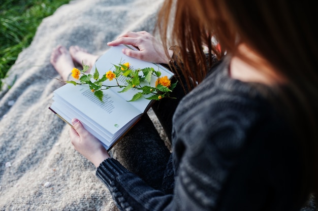 Giovane ragazza bruna seduta sul plaid e leggere il libro.