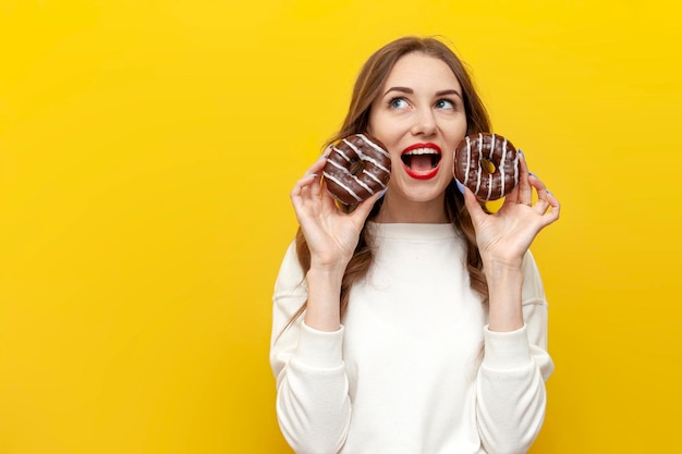 giovane ragazza carina con due ciambelle al cioccolato su sfondo giallo isolato donna che urla