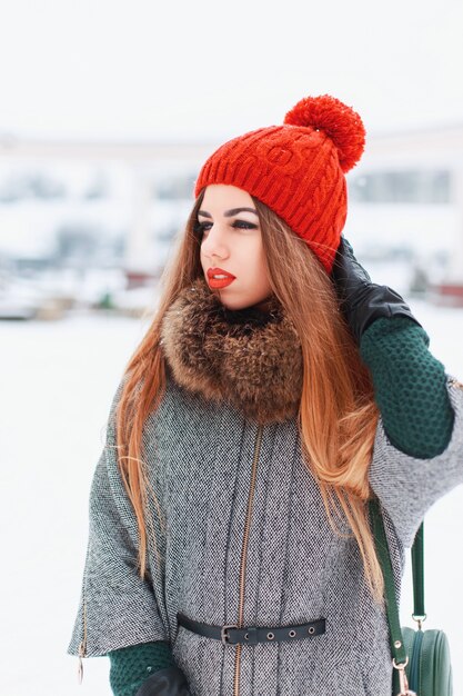 Giovane ragazza carina con un bel sorriso in un cappello e un cappotto lavorato a maglia rosso in una giornata invernale