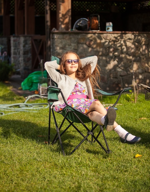 Giovane ragazza carina in occhiali da sole che prende il sole in cortile