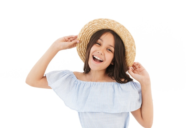 Giovane ragazza castana allegra in vestito e cappello di paglia che posano sul bianco