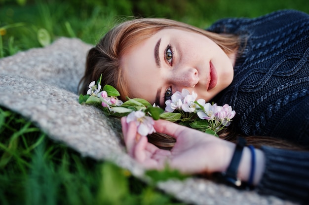 Giovane ragazza castana che si trova sull'erba verde con i rami dell'albero del fiore.