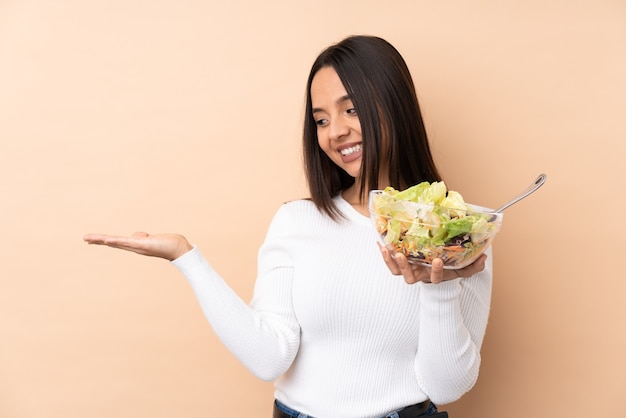 Giovane ragazza castana che tiene un'insalata sopra il copyspace isolato della tenuta immaginario sul palmo per inserire un annuncio