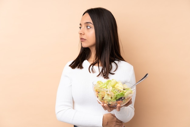 Giovane ragazza castana che tiene un'insalata sopra il ritratto isolato del fondo