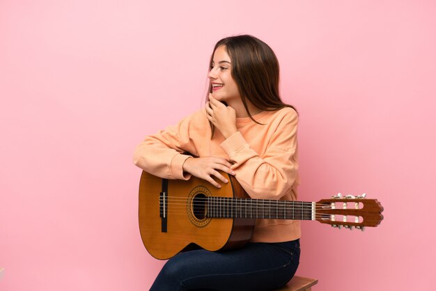 Giovane ragazza castana con il fondo della chitarra che guarda lato