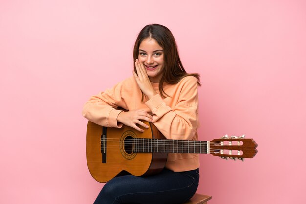 Giovane ragazza castana con la chitarra sopra il sussurro rosa isolato qualcosa