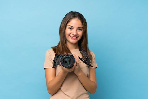 Giovane ragazza castana sopra il blu isolato con una macchina fotografica professionale