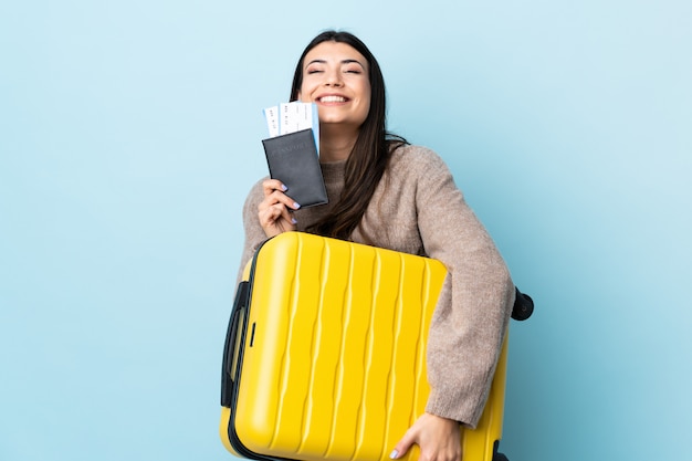 Giovane ragazza castana sopra il blu isolato in vacanza con la valigia e il passaporto