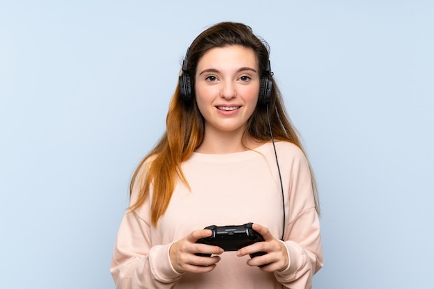Giovane ragazza castana sopra la parete blu isolata che gioca ai videogiochi