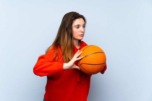 Giovane ragazza castana sopra la parete blu isolata con la palla di pallacanestro