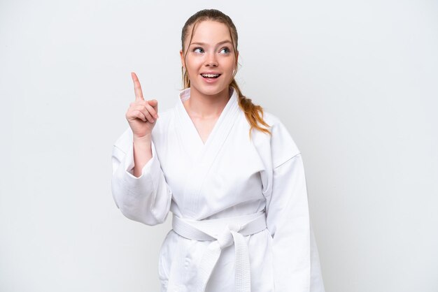 Giovane ragazza caucasica che fa karate isolato su sfondo bianco pensando un'idea che punta il dito verso l'alto