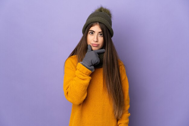 Giovane ragazza caucasica con cappello invernale isolato su sfondo viola pensando