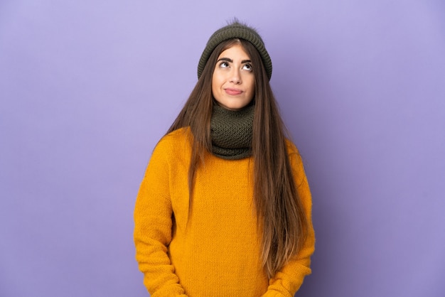 Giovane ragazza caucasica con cappello invernale isolato sulla parete viola e alzando lo sguardo