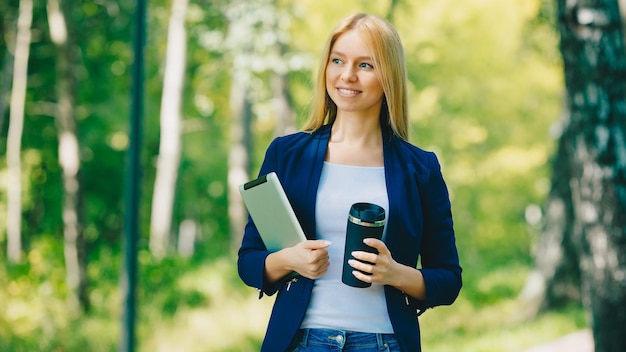 Giovane ragazza caucasica con cuffie wireless nel parco utilizzando tablet e sorridente