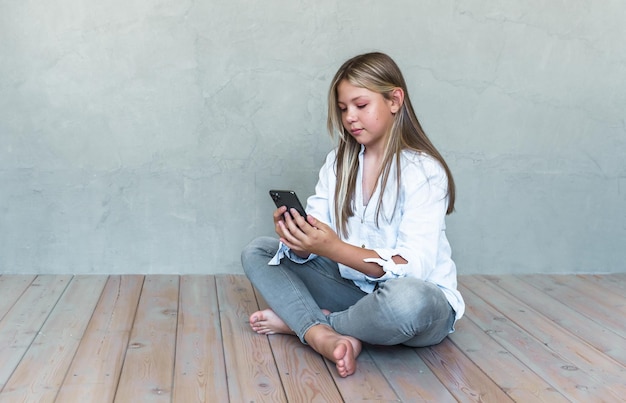 Giovane ragazza caucasica con pelle abbronzata e capelli biondi che utilizza auricolari wireless per chiamare un amico tramite smartphone che tiene il cellulare